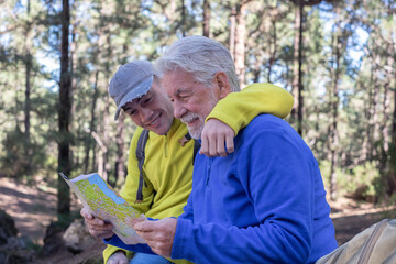 Young grandson and old grandfather consulting trail map while hiking in mountain forest enjoying nature and healthy activity. The new and old generation share the same passion. Adventure has no age