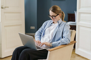 An elegantly poised woman concentrates on her laptop work, draped in a light blue blazer, with...