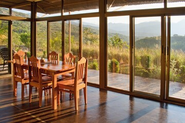 Wooden table in the house interior. Large glass windows and view into the landscape.
