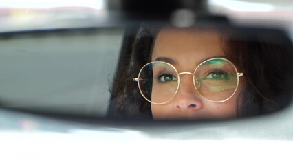 Pretty young woman in glasses drives a car and looking in rearview mirror. Slow motion. Close up...