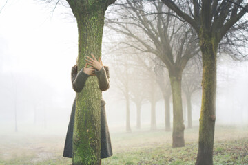 hands touch the trunk of a tree, embracing it in a grove surrounded by fog