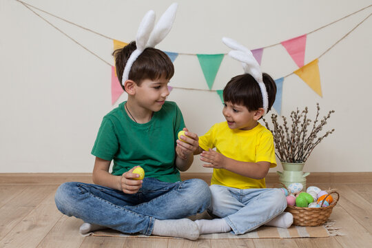 Children in bunny ears hold Easter eggs in their hands and laugh.