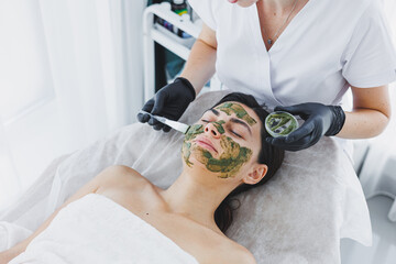 A cosmetologist applies a medical mask to the skin of a woman lying on a couch. Facial. Facial skin...