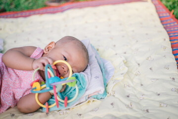 Esther Title: Infant Baby Girl is laying on her back in a pink bodysuit with a development toy for teething.