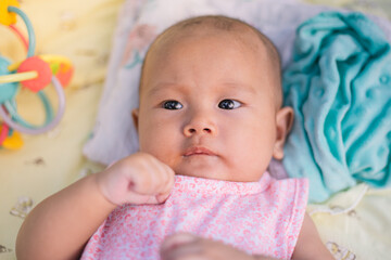 Infant Baby Girl is laying on her back in a pink bodysuit with a development toy for teething.