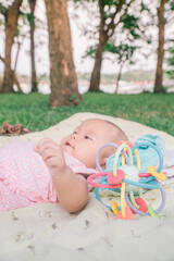Infant Baby Girl is laying on her back in a pink bodysuit with a development toy for teething.