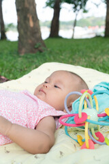 Infant Baby Girl is laying on her back in a pink bodysuit with a development toy for teething.