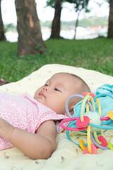 Infant Baby Girl is laying on her back in a pink bodysuit with a development toy for teething.