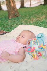 Infant Baby Girl is laying on her back in a pink bodysuit with a development toy for teething.