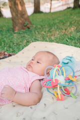Infant Baby Girl is laying on her back in a pink bodysuit with a development toy for teething.