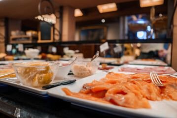 Buffet spread with citrus dessert and sliced salmon on white plate in warm, inviting restaurant or...