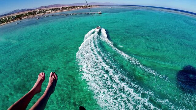 Parasailing point of view couple feet above blue turquoise ocean waters flying, water sports in slow motion perspective