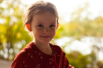 small beautiful girl in a red shirt against a background of blurred foliage
