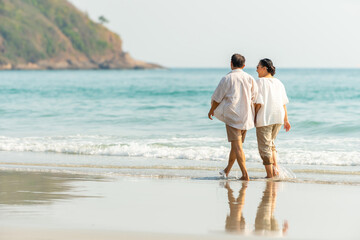 Happy Asian family senior couple walking together on tropical island beach at summer sunset. Retired elderly people relaxing and enjoy outdoor lifestyle travel nature ocean on holiday vacation. © CandyRetriever 