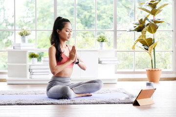 Asian woman practice yoga meditation exercise at home by online training class, Young asia female sitting on mat for relaxed yoga posture , exercise at home, wellbeing, mental health care