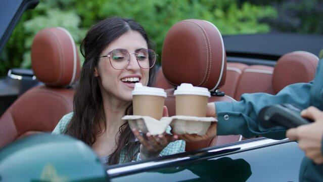 Happy woman receiving coffee in car at drive-thru