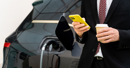 Electric car concept. Businessman checks his phone waiting.