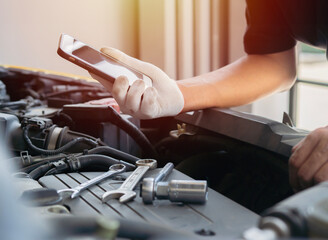 Shot of professional technician car mechanic man's hand hold a mobile cell phone browsing fix...