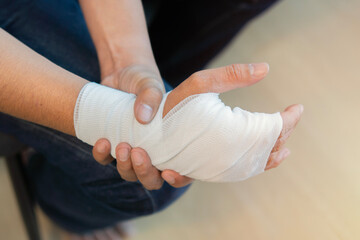 Wrapping wrist and arm with bandage around injured man's  hand at home. First aid