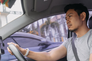 Side view of asian man driving a car and staring the road while traveling alone, going to work, bad traffic jam. - obrazy, fototapety, plakaty