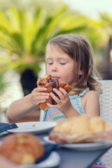 A beautiful little girl eats a croissant with chocolate with appetite