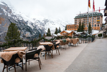 Alpine terrace with modern wicker chairs, fur throws, and wooden tables, overlooking snow covered...
