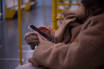 A young woman rides in a modern subway car with a phone in her hands. A beautiful girl in a jacket...