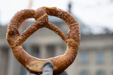 Hand holding Appetizing traditional Bavarian pretzel with the salt crystals. The Berlin Reichstag...