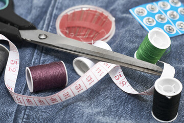 Fototapeta na wymiar scissors needles measuring tape and thread on the background of torn jeans the concept of reasonable consumption of needlework for small businesses