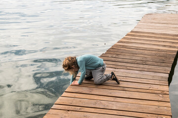 Little boy on wooden boardwalk leading into lake waters