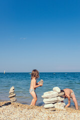 Fototapeta na wymiar Children play on the seashore. A little girl and boy play with stones on the beach on a sunny summer day
