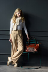 beautiful curly blond hair woman posing with a brown shopper bag near gray wall