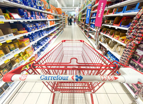 Pusty koszyk, w&oacute;zek sklepowy w supermarkecie, rozmazane tło, wnętrze sklepu, supermarketu, w&oacute;zek na zakupy, p&oacute;łki sklepowe z produktami. Hipermarket Carrefour. Warszawa, CH Arkadia. Miejsce na tekst