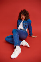 young african american female model in denim attire looking at camera and posing on red background