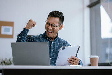 Successful business man, excited young man Keeping up arms and showing positive emotions, happy working in modern office on computer.