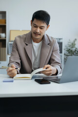 Businessman sitting at a table at office working on a laptop and writing down ideas in a notebook.