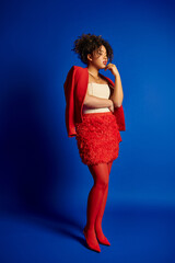 good looking stylish african american female model in vibrant outfit looking away on blue backdrop - 781174289
