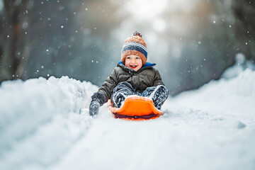Fototapeta na wymiar Smiling little kid riding on orange snow slides in winter time