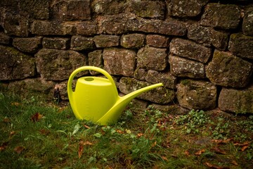 Yellow watering can on the grass in front of the stone wall