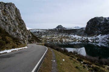 Scenic view of a road along a lake against a rocky mountain range covered with snow