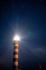 Vertical low angle shot of bright light on the top of lighthouse against blue starry night sky