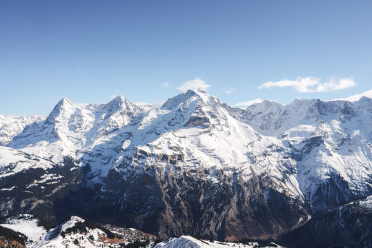 Experience the awe inspiring Swiss Alps with snow covered peaks and rugged slopes captured from the Murren ski resort. Majestic mountains under a clear blue sky create a dramatic alpine scene.