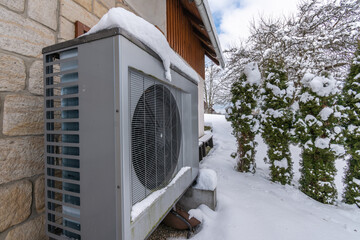 Air heat pump covered with snow beside house in winter