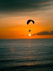 Silhouette shot of a person paragliding above a coast on a sunset