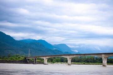 Fototapeta na wymiar Countryside bridge over the river with mountains and the cloudy sky in the background