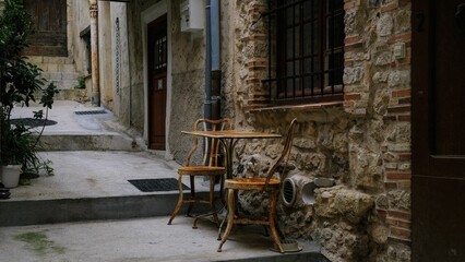 Fototapeta na wymiar Table and two chairs on the narrow street in front of a house, with stairs in the background