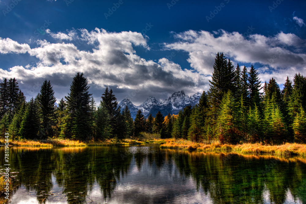 Canvas Prints Mountain range reflecting in a tranquil lake surrounded by lush evergreen trees under a dramatic sky