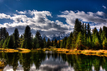 Mountain range reflecting in a tranquil lake surrounded by lush evergreen trees under a dramatic sky