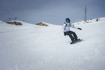 Winter sports enthusiast snowboarding down a snowy slope at a developed ski resort with a ski lift...