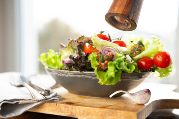 Fresh green salad in a ceramic bowl with tomato, onions and olives on wooden cutting board. Healthy nutrition concept for fitness and spring diet. Close-up.